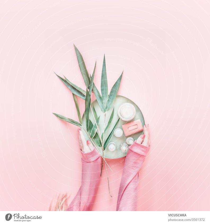 Frauenhände in rosa Kapuzenpulli mit Naturkosmetikprodukten und Bambusblättern auf pastellrosa Hintergrund. Moderne Hautpflege. Null Abfall. Flach liegend.  Layout eines Schönheitsblogs. Ansicht von oben