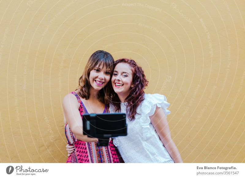 zwei Freundinnen oder Schwestern, die ein Foto im Freien mit einem Mobiltelefon über gelbem Hintergrund machen. technologie- und lebensstilkonzept Freunde Handy