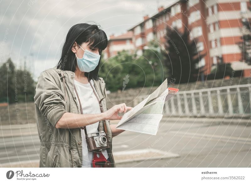 Frau mit medizinischer Maske, die mit einer Kamera auf einen Stadtplan schaut Coronavirus Junge Frau Virus Seuche Reisender reisend Tourist Tourismus Feiertage