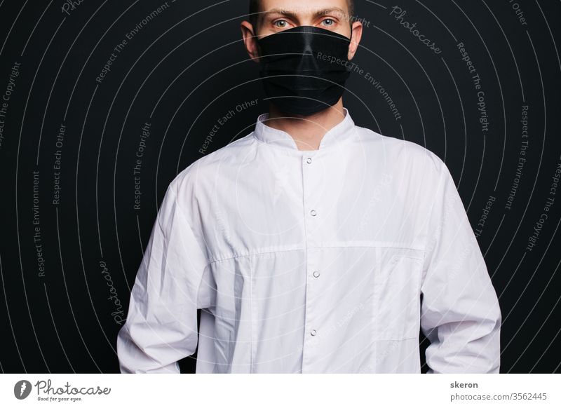 junger Arzt mit kurzen Haaren im Ärztekittel trägt eine schwarze Schutzmaske. männlicher Laborant im Schutzanzug bei der Arbeit mit Patienten mit Coronavirusinfektion während der Pandemie.