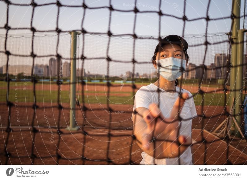 Junge Frau mit Schutzmaske steht hinter Netzzaun auf Sportplatz Mundschutz Coronavirus Sportpark Zaun Einschränkung verhindern behüten COVID jung sportlich