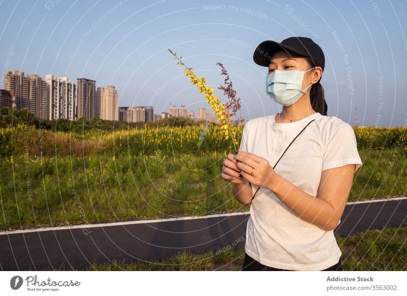 Ethnische Frau mit medizinischer Maske steht auf grünem Feld Mundschutz behüten Coronavirus verhindern COVID Natur jung lässig ethnisch modern Sicherheit
