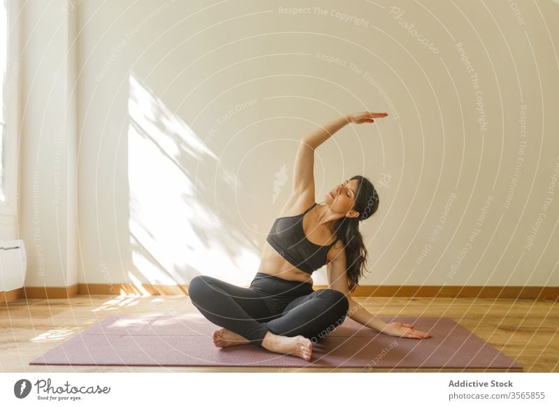 Flexible Frau macht Seitenbeuge und praktiziert Yoga Seitenknick üben Übung beweglich Achtsamkeit Gelassenheit sukhasana Wohnzimmer Dehnung heimwärts ruhig