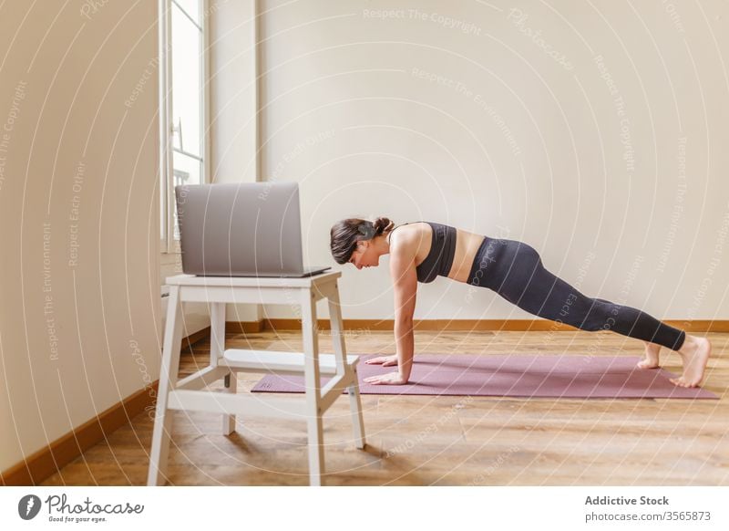 Passgenaue Frau, die zu Hause in Plankenpose steht Plankenhaltung Yoga üben Wellness heimwärts Gesunder Lebensstil Fitness Laptop Unterlage benutzend Gerät