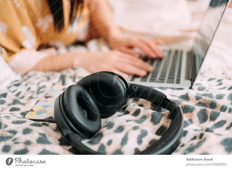 Nutzfrau, die mit Kopfhörern am Laptop surft Frau Smartphone Bett Kälte heimwärts Wochenende Komfort benutzend Tippen Browsen Keyboard Lügen Lifestyle