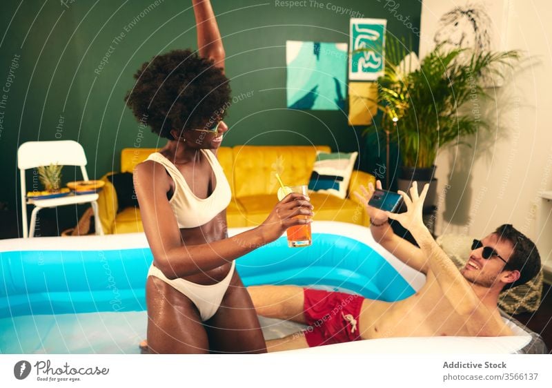 Zufriedenes multiethnisches Paar beim Fotografieren und Entspannen im Pool fotografieren sich[Akk] entspannen aufblasbar Party zu Hause bleiben Cocktail