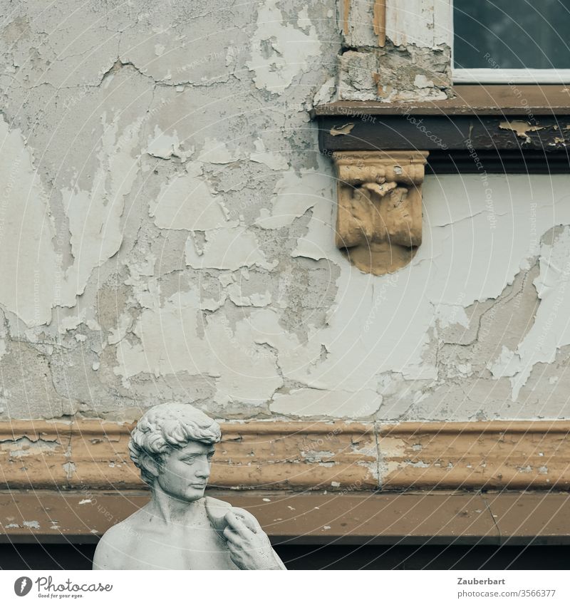 Kopf einer männlichen Statue vor Fassade mit abblätternder Farbe und Stuck-Detail eines Fensters römisch Rom braun grau alt Fensterrahmen Mauer Verfall