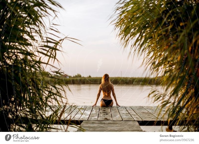 Junge Frau im Bikini auf einem Pier am See sitzend allein attraktiv Strand schön Schönheit blond sorgenfrei Kaukasier Model Natur im Freien Person posierend