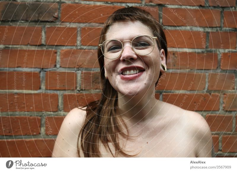 Portrait einer lachenden jungen Frau vor einer Backsteinwand Jugendliche schön stark alternativ groß Piercing Haut intensiv Blick schauen beaobachten stehen