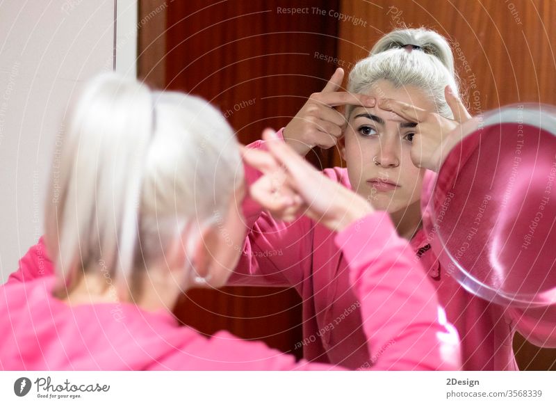 Frau im Bademantel, die einen Pickel im Gesicht in den Spiegel schaut und versucht, ihn zu drücken. Person Schönheit Akne Haut Pflege Erwachsener jung Blick