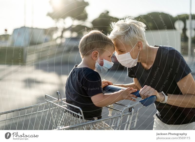 Mutter spielt fröhlich mit dem Kind, das im Einkaufswagen sitzt. Beide tragen eine schützende Gesichtsmaske. Frau Mundschutz spielen Karre Werkstatt Baby