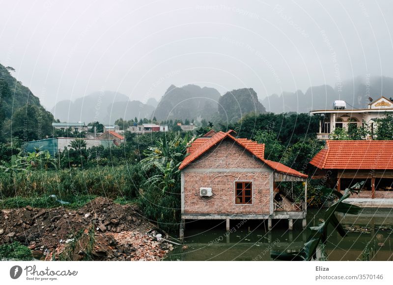 Landschaft mit Häusern in Vietnam nebelig Ninh Binh Wasser Stelzen grün Südostasien Kalksteinfelsen Dächer Dorf Asien