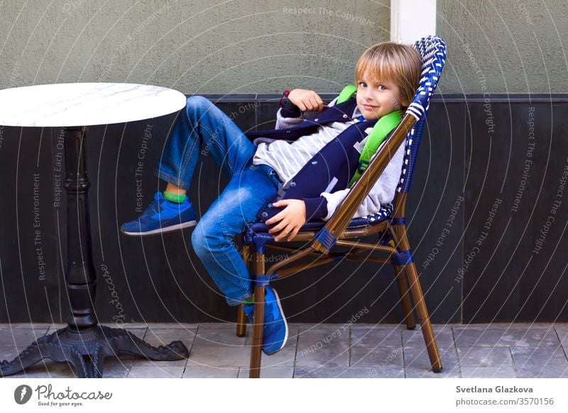 Der Junge sitzt auf einem Stuhl in einem Stadtcafé. jung im Cafe Café im Cafe sitzend Personen-Couchtisch Hipsters-Restaurant Familienrestaurant Kind Großstadt