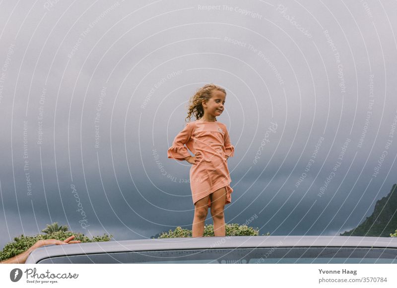 Kind steht auf einem Autodach und der Wind weht ihr das Haar zurück Hawaii Sturm Strand Himmel Küste Wolken Farbfoto Natur Außenaufnahme Landschaft Unwetter