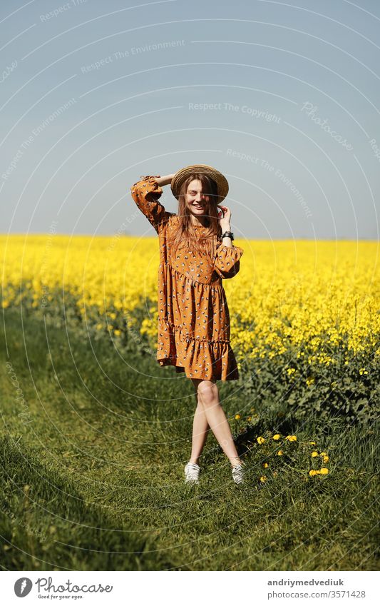 stilvolle junge Frau mit Strohhut in einem Feld mit gelben Blumen. Mädchen im Blütenkleid. Hintergrund mit gelben Blumen und blauem Himmel Porträt Mode Frühling