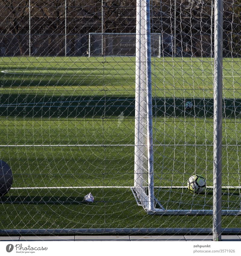Blick längs des Fussballfeldes von Tor zu Tor. Das vordere Tor ist angeschnitten, ein Ball liegt hinter der Linie, weite seitliche Schattenwürfe auf das Spielfeld