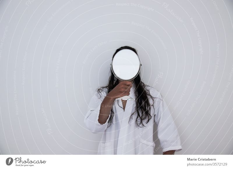Konzeptionelles Foto eines langhaarigen Mannes in weißer Robe, der einen Spiegel vor dem Gesicht hält Begriffsbild Identitätskonzept Anonymität