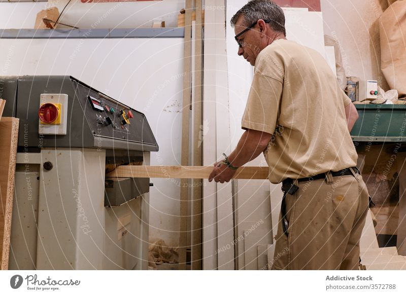 Sorgfältig nachdenklicher Holzarbeiter beim Hobeln von Holzbalken mit der Maschine in einer zeitgenössischen Werkstatt Meister Holzarbeiten Grinden Zimmerer