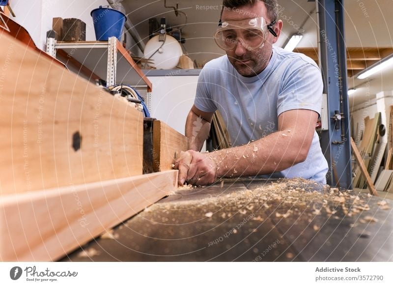 Holzfacharbeiter mit Fräse bei der Arbeit mit Holz in einem modernen Arbeitsraum Zimmerer Fräsen Maschine Brille Werkstatt Sägemehl Sicherheit Mann
