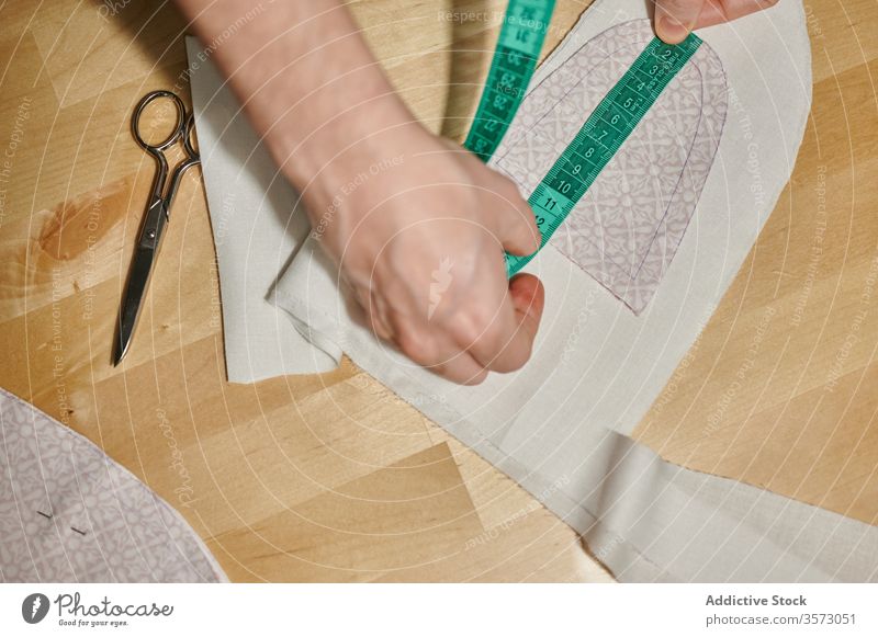 Nicht erkennbarer Designer misst Textildetails mit Klebeband Spielfigur Gewebe messen Material Muster Detailaufnahme nähen Schere hölzern Tisch heimwärts Stoff