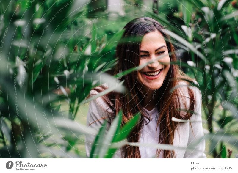 Junge hübsche Frau lacht herzhaft inmitten von grünen Pflanzen draußen im Garten jung lachen lebensfreude Natur Spaß Porträt Glück Fröhlichkeit südländisch