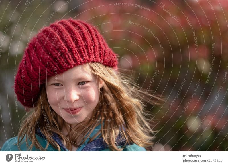 Das Mädchen mit der Mütze portrait winter mütze strickmütze Winter Gesicht lachen Farbfoto Freude lange haare Wind in den Haaren (sofern vorhanden) rot stricken