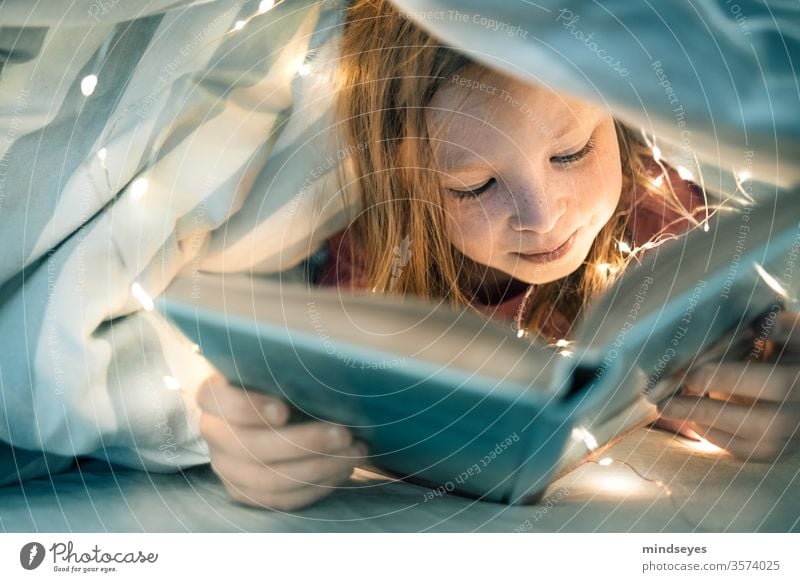 Mädchen liest Buch unter der Decke Kind Portrait lesen buch bett bettdecke lichterkette kindheit heimlich versteckt spannend Farbfoto lernen Innenaufnahme