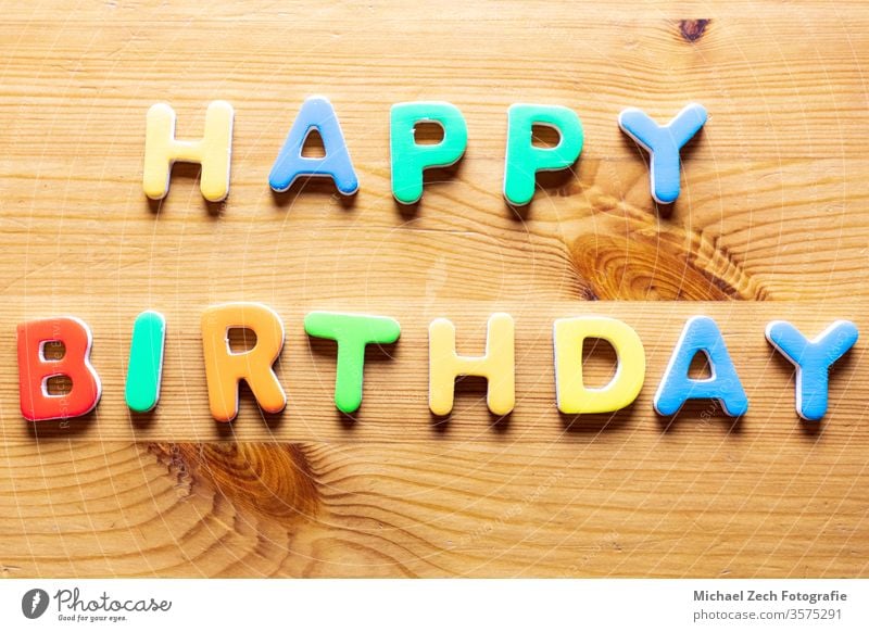 Mit bunten Buchstaben geschriebene Happy Birthday-Worte auf Holzuntergrund Brief Feiertag Geburtstagsfeier horizontal Spaß Postkarte heiter Bändchen Glückwunsch