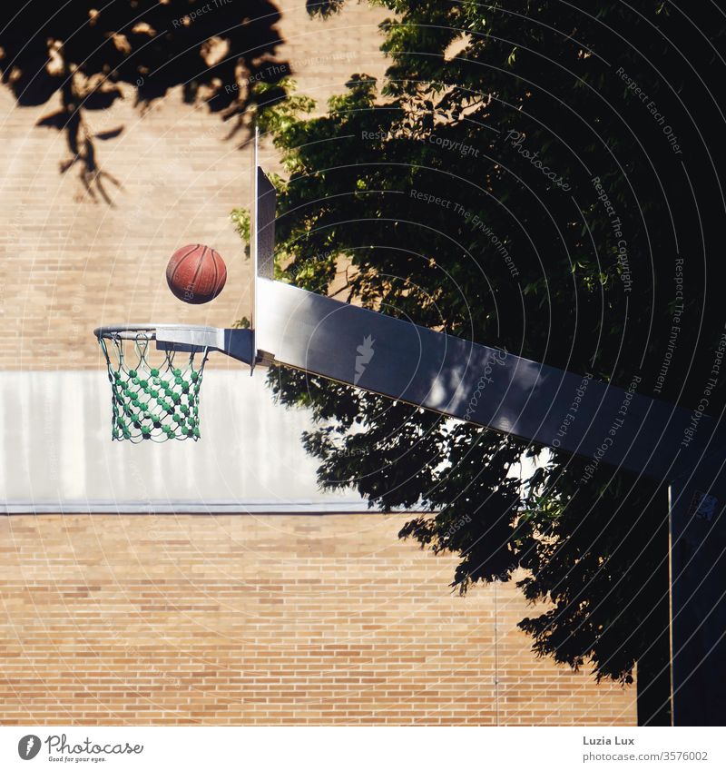 Basketball, roter Ball im Flug auf den Korb Basketballkorb Wand Netz Fassade Farbe Backstein Backsteinwand Backsteinfassade menschenleer Mauer Außenaufnahme