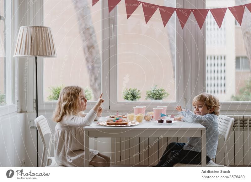 Kleine Kinder sitzen am Tisch am Fenster im Wohnzimmer heimwärts feiern Geburtstag Kuchen Geschwisterkind Zusammensein Girlande gemütlich süß Feiertag essen
