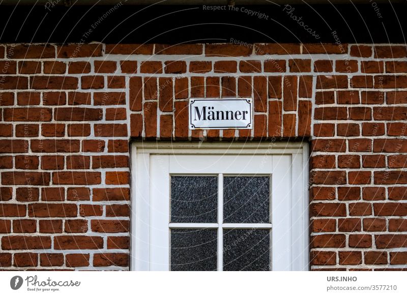 Text auf einem Emaileschild über einer Tür mit Sprossenfenster  trägt die Aufschrift Männer Backsteinwand Fassade Schriftzug Schriftzeichen Mauer Buchstaben
