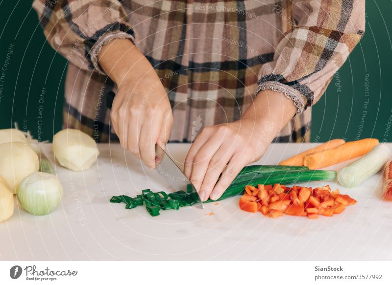 Frau schneidet frische grüne Zwiebel in ihrer Küche auf weißem Marmor, um ihr Essen zuzubereiten. sich[Akk] schälen Gemüse Paprika rot Kartoffeln Veganer