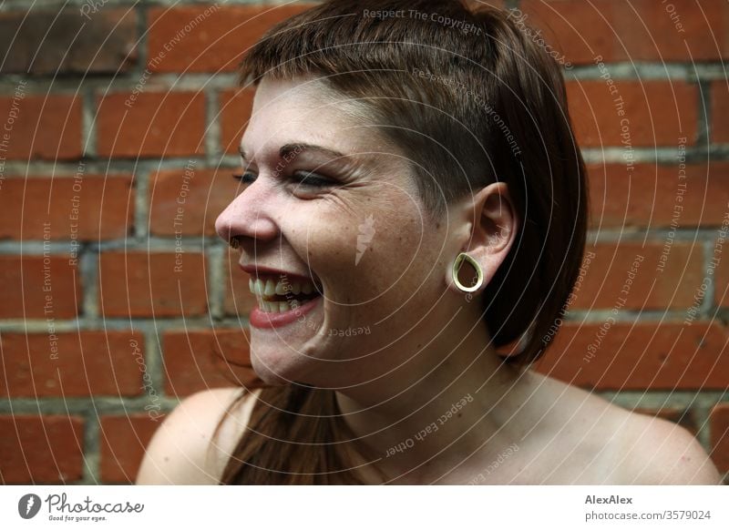 Portrait einer lachenden, jungen Frau vor einer Backsteinwand Spaß frei wild Freude heiter zuversichtlich Vertrauen Textfreiraum rechts Coolness