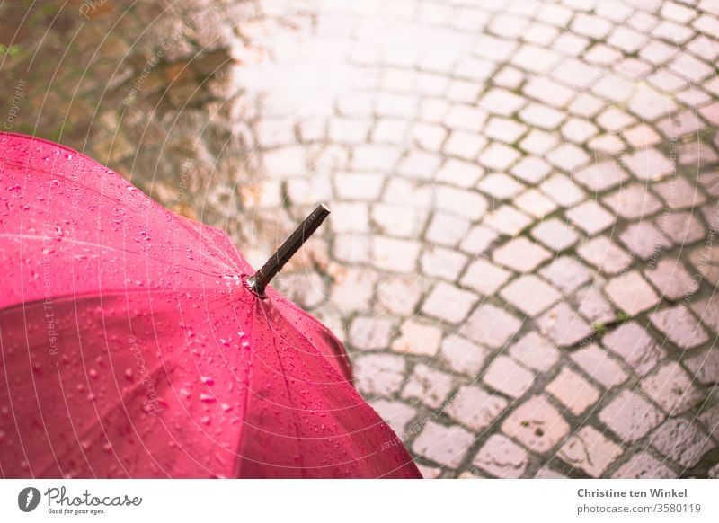 Regenschirm in pink und Naturstein - Pflaster, nass und glänzend magenta Schirm Pfütze Pflastersteine Natursteinpflaster Porphyr kalt Steinboden