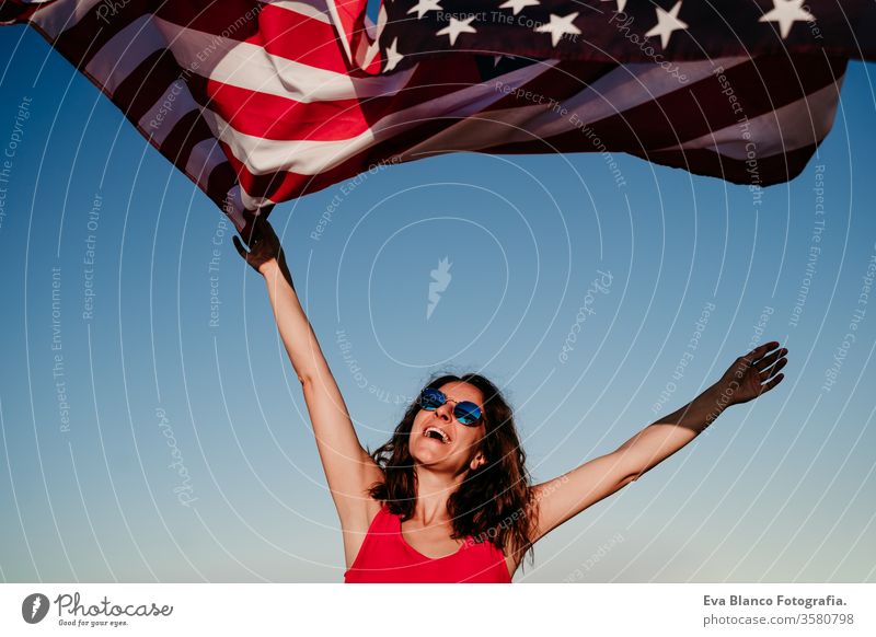 junge Frau, die bei Sonnenuntergang die Flagge der Vereinigten Staaten im Freien hält. Unabhängigkeitstag in Amerika, Konzept des 4. Juli Vereinigte Staaten
