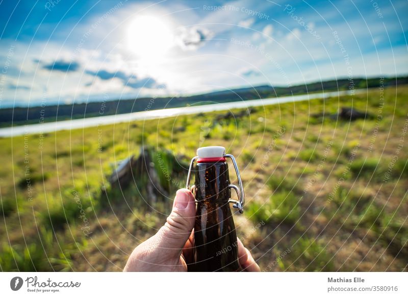 Genießt das Leben. Prost! Flasche Flaschenhals Bierflasche Bügelverschluss Büro Sonne Gegenlicht See Bierchen trinken Getränk Glasflasche Hand öffnen Biergarten
