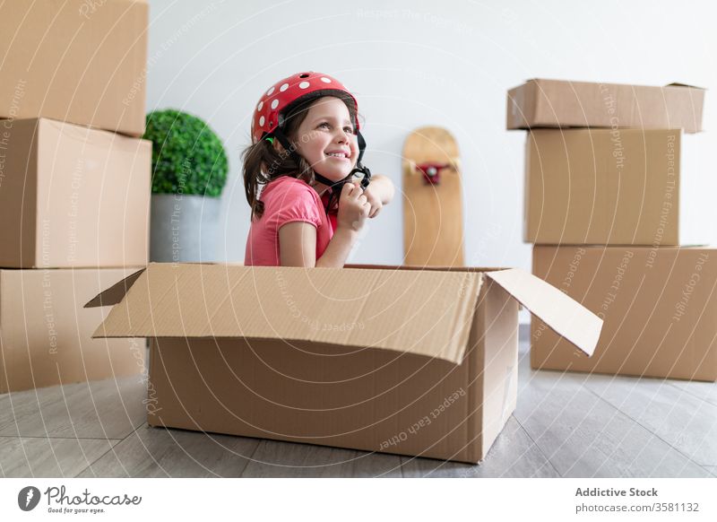 Fröhliches Mädchen spielt in Kartonschachtel spielen Kasten Lächeln Schutzhelm befestigen sitzen bewegend verlegen Spaß Vorstellungskraft Kind Phantasie Glück