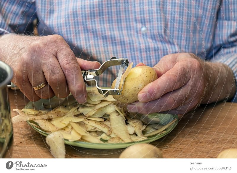 Männerhände mit Schälmesser: Senior in blau-karierten Hemd schält Kartoffeln am Tisch Hände Mann Senioren schälen Teller Ehering Lebensmittel Hand Ernährung