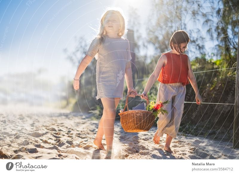 Kleine Mädchen, die barfuß über den Sand laufen und gemeinsam einen Picknickkorb pflegen. Sommerfreizeit, Liebe und Freundschaft. Natur Spaziergang Park Kind