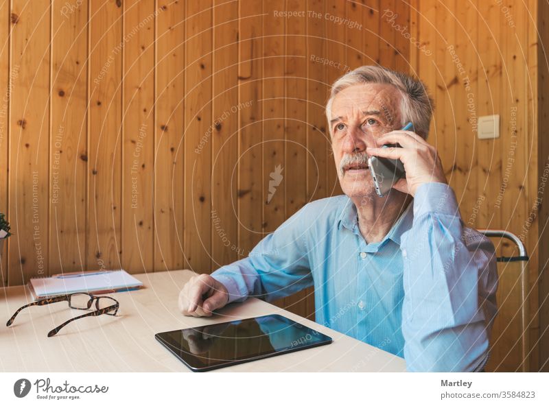 Großvater im Gespräch mit seinen Enkeln und Verwandten, die von zu Hause unter Quarantäne gestellt wurden, über das Coronavirus. Älterer Mann benutzt Smartphone und Tablet in seinem Büro