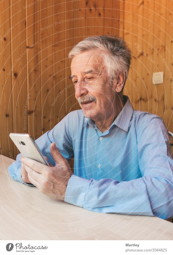 Glücklicher grauhaariger älterer Mann, der ein Smartphone benutzt und während des Coronavirus einen Videoanruf bei seinen Enkelkindern oder seiner Familie zu Hause tätigt. Er schaut sich lustige Videos in sozialen Netzwerken an.