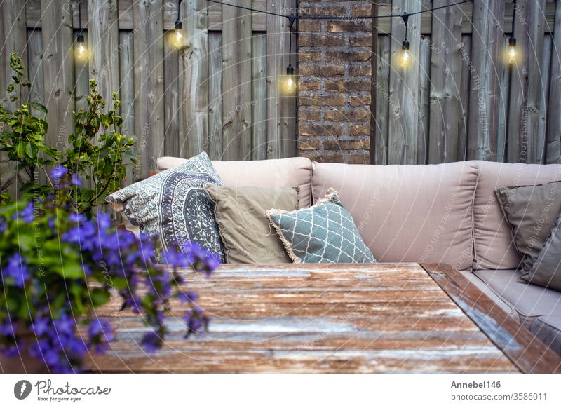 Stilvolle Gartenmöbel im Freien, Sofa mit Kissen und Lampen, hängende Glühbirnen, gemütliche moderne Ecke auf der Terrasse Blume Hintergrund Familie Spa Design
