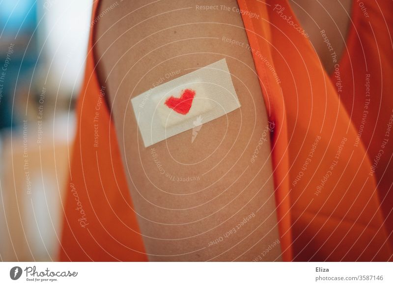 Ein Pflaster mit einem kleinen roten Herzen darauf auf dem Oberarm einer Frau. Konzept Impfung und Fürsorge. Verletzung trösten haut Liebe Schmerz Gefühle Wunde