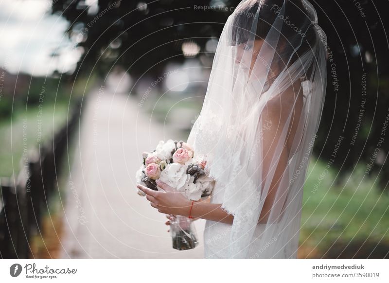 Schöne junge Braut in einem weißen Luxuskleid und in einem Brautschleier mit einem Blumenstrauß, der im Freien posiert. hochzeitsporträt. kopierraum Hochzeit