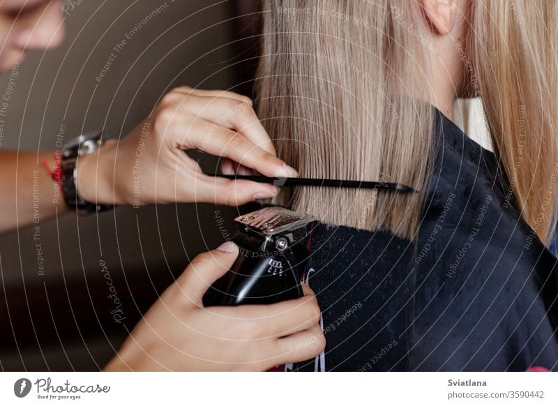 Der Friseur macht einen modischen Haarschnitt für ein Mädchen mit einem Haarschnitt. Behaarung Salon Maschine Hand professionell Mode Stil geschnitten Klient