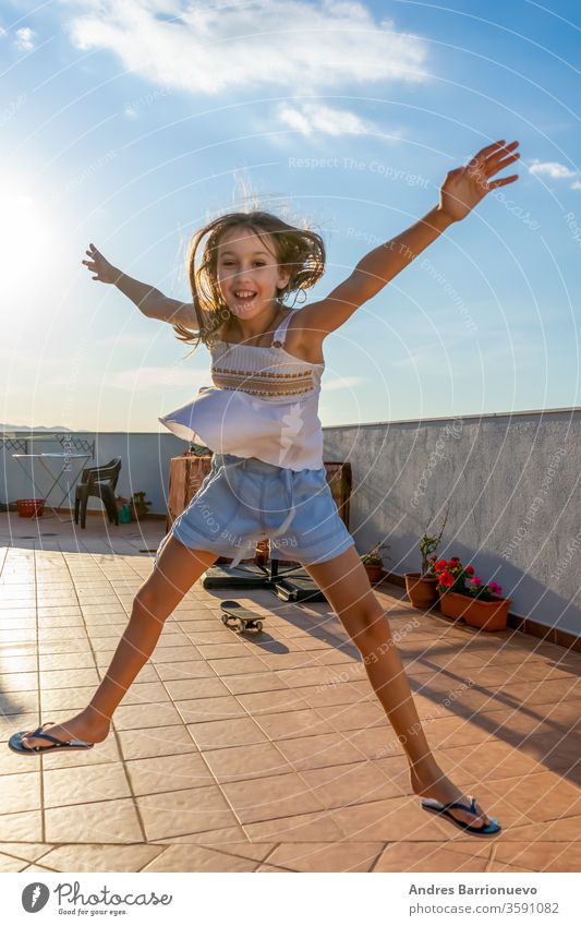 Hübsches kleines Mädchen in weißem Tanktop, das bei Sonnenuntergang auf der Terrasse des Hauses tanzt und springt Natur Fröhlichkeit Himmel schön Spielen
