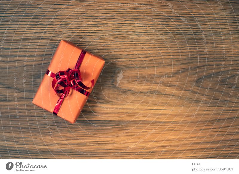 Ein verpacktes Geschenk mit rotem Geschenkband auf Untergrund aus Holz Verpackung Geburtstag Weihnachten Weihnachtsgeschenk Geburtstagsgeschenk rosa Vorfreude