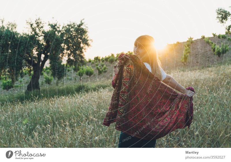 Porträt eines schönen lächelnden Mädchens, das sich in der Natur mit einem Sarong in einem Feld bei Sonnenuntergang erfreut. Frau Sommer Lebensstile sonnig jung
