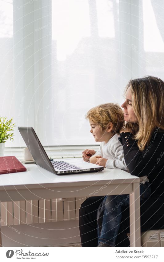 Frau mit kleinem Kind arbeitet zu Hause am Laptop Arbeit heimwärts Mutter benutzend Zusammensein online beschäftigt abgelegen neugierig Punkt Mutterschaft