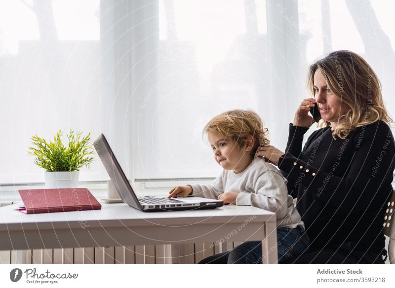 Frau mit kleinem Kind arbeitet zu Hause am Laptop Arbeit heimwärts Mutter benutzend Zusammensein online beschäftigt abgelegen neugierig Punkt Mutterschaft